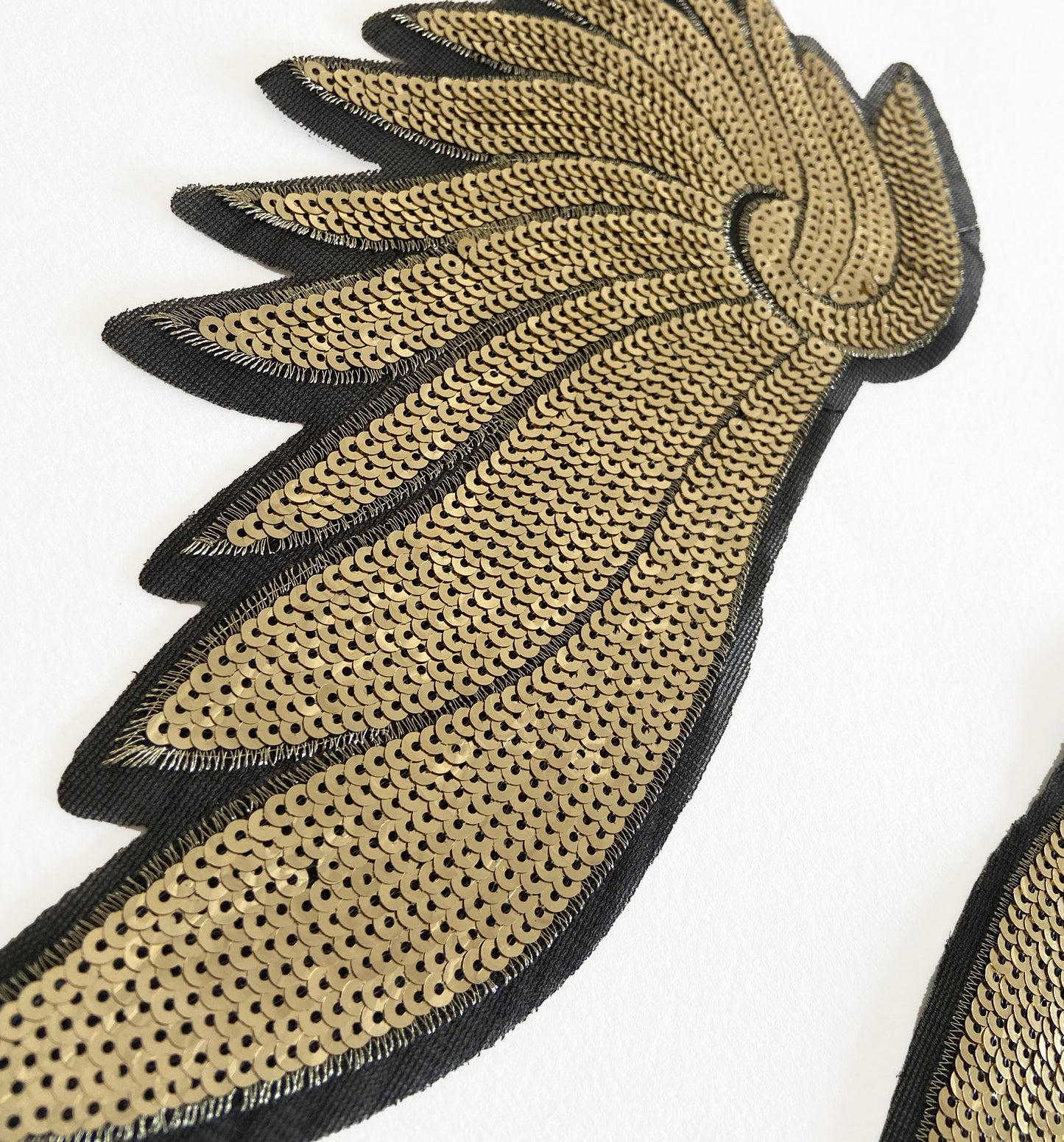 Decorative feather-shaped patch with gold and black details on a white background