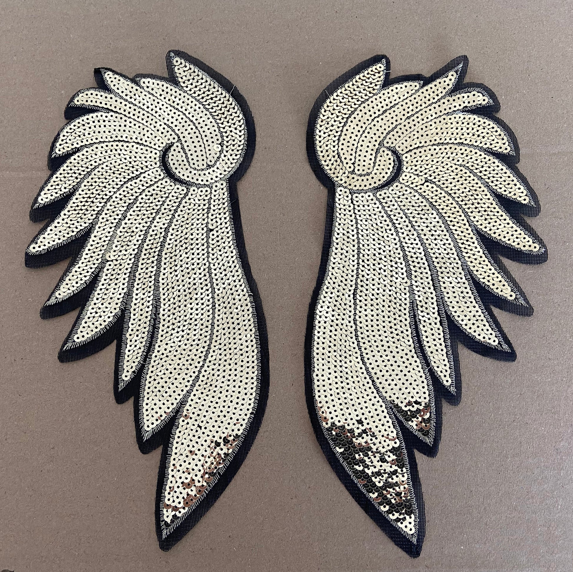 Pair of wing-shaped decorative patches with sequin details on a brown background