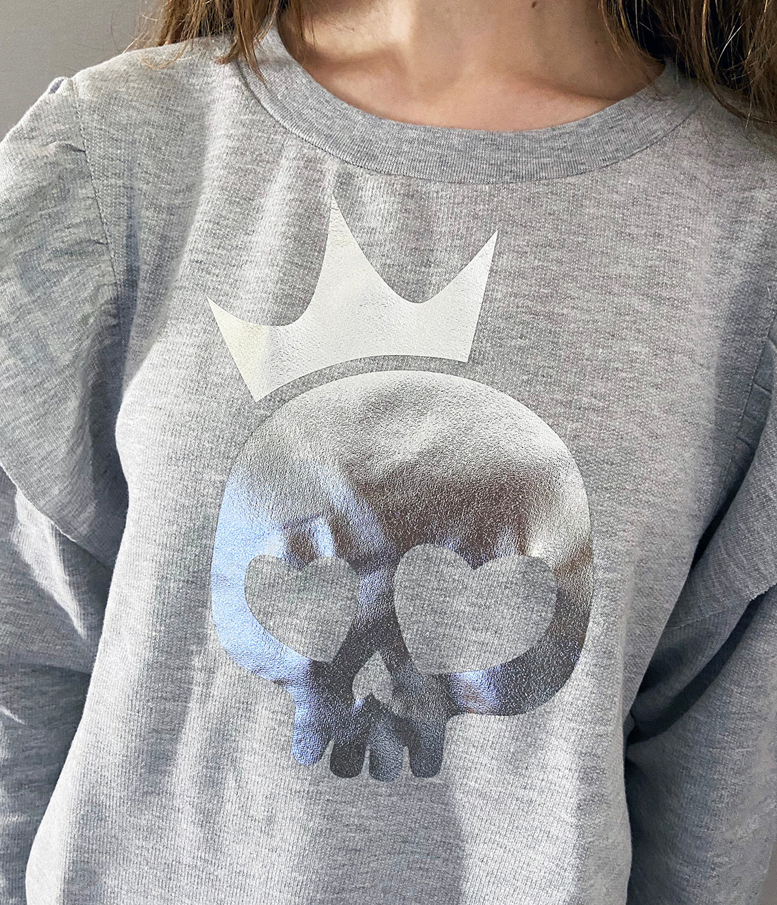 Close up of a person wearing a light grey shirt with silver foil skull print.