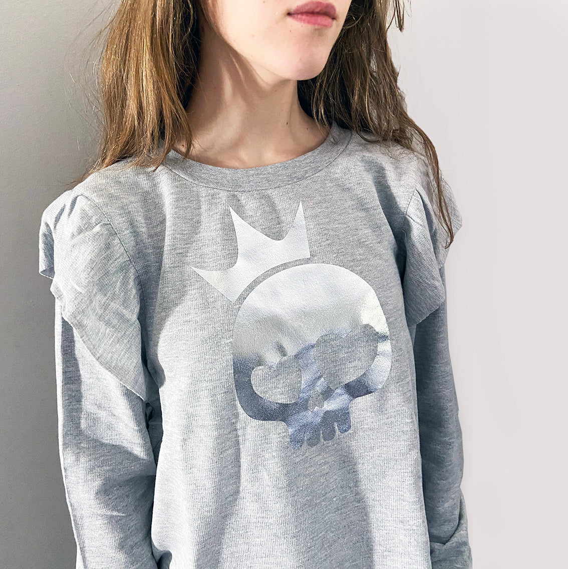 a person wearing a light grey shirt with silver foil skull print.