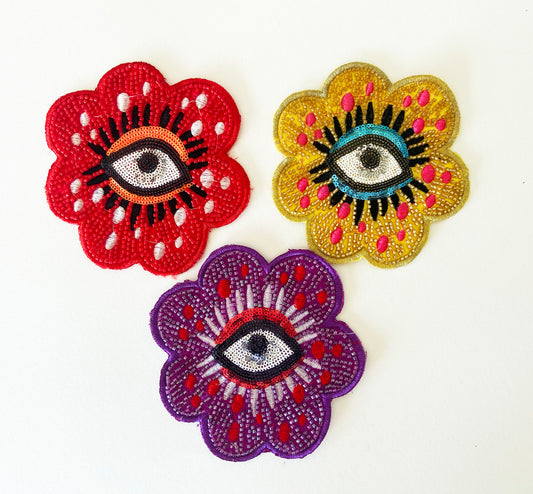 Three colorful flower-shaped patches with eye designs on a white background